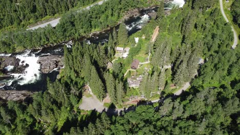 Distant-aerial-view-of-Voss-zipline-and-climbing-park-besides-strandaelvi-river-in-Voss-Norway---Lush-green-summer-aerial-with-river-flowing-nicely-besides-park