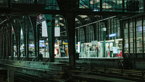 Inside-Berlin-Friedrichstrasse-subway-station-with-commuters-and-trains-speeding-nightlife-illuminated-time-lapse