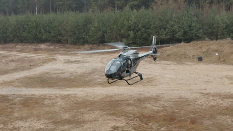 Vista-Aérea-De-Un-Helicóptero-Militar-Con-Un-Soldado-Sosteniendo-Un-Rifle-De-Francotirador-Flotando-Sobre-El-Campo-De-Entrenamiento,-Disparo-De-Un-Dron