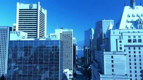 Drone-flyover-Vancouvers-Burrard-Street-towards-Robson-150-feet-above-the-ground-level-over-Fairmont-hotel-VIP-balcony-across-office-towers-mirrored-glass-window-reflections-clear-sky-green-trees2-5