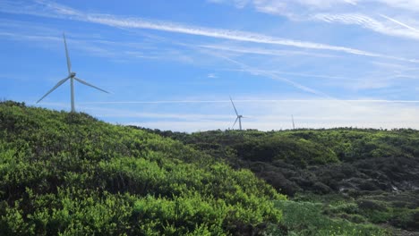 Tres-Turbinas-Eólicas-Moviéndose-Con-Dunas-De-Arena-En-Primer-Plano,-Una-Turbina-Averiada