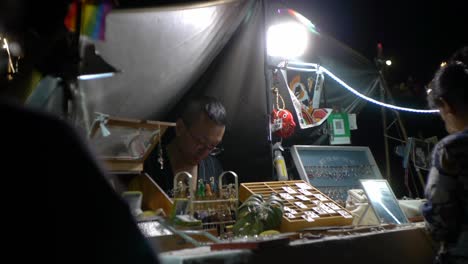 Asiatischer-Mann,-Der-Als-Schmuckverkäufer-Auf-Dem-Nachtmarkt-Im-Freien-Arbeitet,-Gefilmt-Im-Handheld-Stil