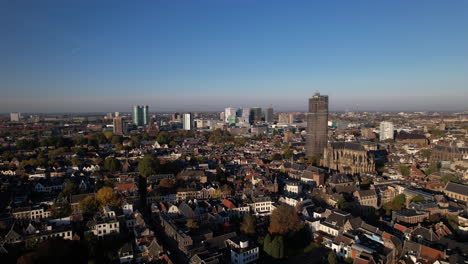 Aerial-approach-of-De-Dom-medieval-cathedral-tower-in-scaffolding-in-Dutch-city-center-of-Utrecht-towering-over-the-cityscape-with-financial-district-and-central-train-station-area-in-the-background