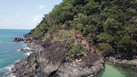 Drone-aerial-pan-up-over-tropical-blue-beach-water-and-rainforest-cliff