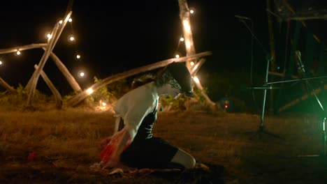 Caucasian-woman-performance-ecstatic-dance-performance-while-seated-on-ground-during-night,-filmed-with-slow-roving-movement