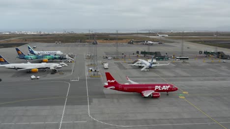 Airline-Play-red-Airbus-320-taxiing-on-tarmac-of-airport,-Boeing-airplanes-parked,-Iceland