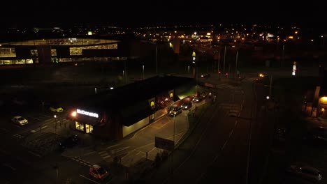 Illuminated-McDonalds-fast-food-drive-through-night-flying-northern-UK-town-aerial-view