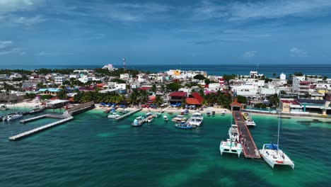 Aerial-view-of-boats,-beaches-and-hotels-on-the-coast-of-Isla-Mujeres,-in-sunny-Mexico---low,-tracking,-drone-shot
