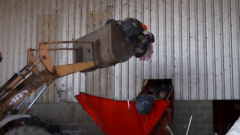 Close-view-of-a-bulldozer's-bucket-dumping-garbage-onto-a-conveyor-belt-in-a-waste-processing-facility