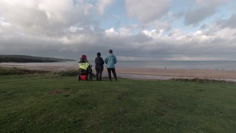 Disabled-pensioner-sitting-with-pair-of-hikers-looking-across-Irish-sea-coastline