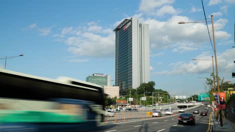 Clouds-movement-time-lapse-over-LG-Electronics-Seocho-Research-and-Development-Campus-Building-and-Yangjae-daero-road-busy-cars-traffic-on-multilane-road-on-summer-day