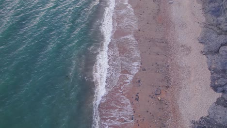 Top-down-drone-shot-of-waves-crashing-on-the-beach,-Jurassic-Coast,-Dorset,-UK
