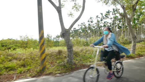 Group-of-4-women-riding-bicycles-on-countryside-roads-during-sunny-day-and-riding-past-camera,-filmed-as-wide-angle-shot-from-left-side-of-cyclists