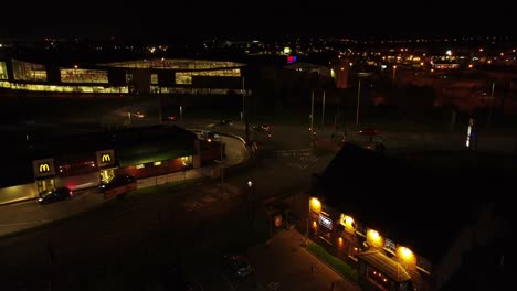 Fliegen-über-Die-Stadtautobahn-In-Uk-Und-Mcdonalds-Fast-Food-Fahren-Durch-Die-Nachts-Beleuchtete-Luftbahn-Rückansicht