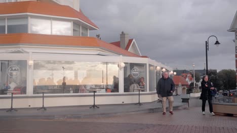 Tourist-couple-walking-onto-sea-promenade-of-De-Haan