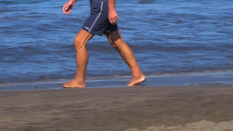 Man-walking-on-the-black-sand-coast-on-a-sunny-summer-day-on-the-beach-of-Playa-De-Las-Americas-,-medium-handheld-shot