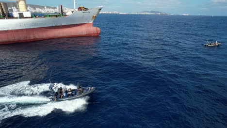 Toma-Aérea-De-Una-Lancha-Rápida-De-La-Policía-Nacional-Que-Pasa-Cerca-De-Un-Barco-Mercante