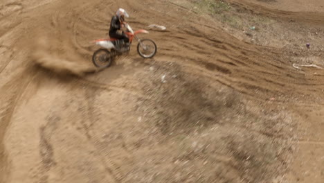 Dynamic-FPV-aerial-view-of-motocross-rider-doing-wheelie-on-dirt-track