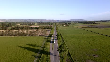 Aerial-view-of-a-large-cargo-truck-driving-down-a-perfectly-straight-road-in-the-countryside