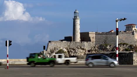 Colorful-vintage-cars-and-other-vehicles-driving-by-the-landmark-lighthouse-at-Faro-Castillo-del-Morro