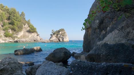 Turistas-Bañándose-En-Aguas-Turquesas-De-La-Playa-Golfo,-Pintoresca-Playa-Rodeada-De-Rocas,-Parga