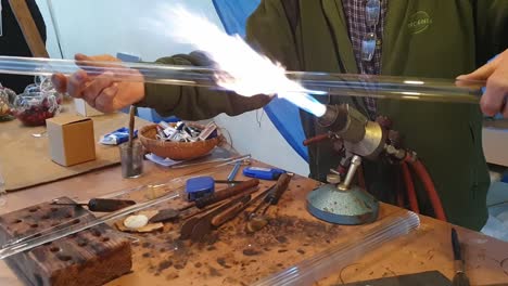 Close-up-of-a-glassblower-artisan-shaping-the-hot-molten-glass-at-strong-fire-inside-a-workshop