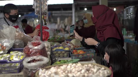 Housewife-with-mask-while-shopping-for-various-vegetables-in-central-market-and-paying-by-online-transaction,-COVID-19-situation