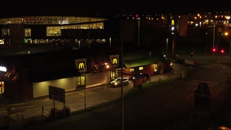 Los-Vehículos-Que-Esperan-Fuera-De-La-Unidad-De-Comida-Rápida-Mcdonalds-Iluminados-Por-La-Noche-En-El-Norte-De-La-Ciudad-Del-Reino-Unido-Vista-Aérea-En-órbita-Ascendente-A-La-Derecha