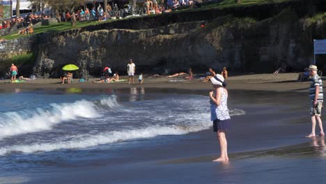 People-enjoying-warm-weather-and-Atlantic-ocean-on-a-sunny-summer-day-on-the-beach-of-Playa-De-Las-Americas-,-medium-handheld-shot