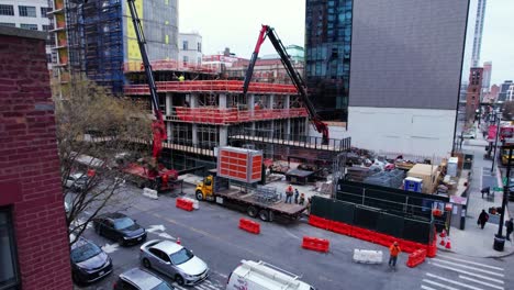 Aerial-view-of-two-red-knuckle-boom-cranes-lifting-construction-materials-in-middle-of-the-city-in-New-York---pull-back,-drone-shot