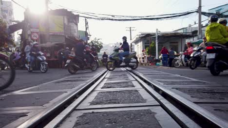 Motorradverkehr-über-Bahngleise-Auf-Einem-Bahnübergang-In-Saigon,-Der-Aus-Einem-Niedrigen-Winkel-Ins-Licht-Blickt