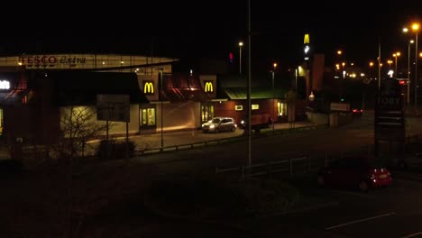 Vehicles-waiting-outside-McDonalds-fast-food-drive-through-illuminated-at-night-in-Northern-UK-town-aerial-view-rising