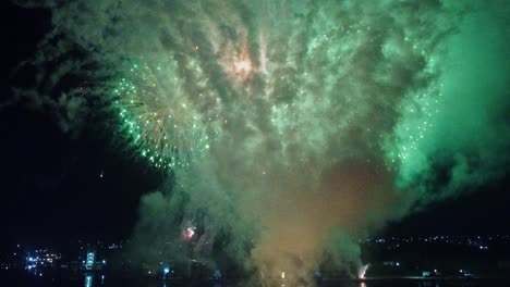 Huge-colorful-firework-in-winter-night-sky-over-city-illuminated-by-lights-filmed-by-drone
