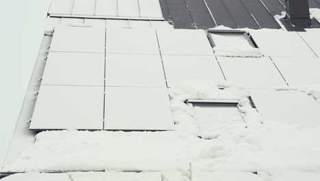 Solar-panel-cells-covered-in-white-snow-on-private-house-rooftop,-tilt-up-view