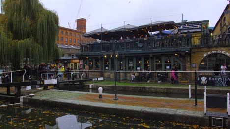 Toma-Panorámica-A-Través-De-La-Famosa-área-De-Camden-Lock-Y-El-Mercado-Con-Compradores-Caminando-En-El-Norte-De-Londres,-Reino-Unido-En-Un-Día-Nublado