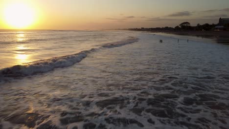 AERIAL:-Drone-shot-of-a-beach-at-sunset-with-people-swimming-in-the-ocean