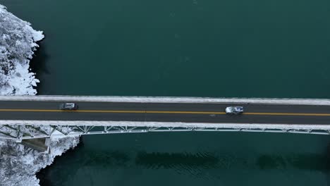 Top-down-aerial-view-of-cars-driving-across-Deception-Pass-State-Park-in-the-snow