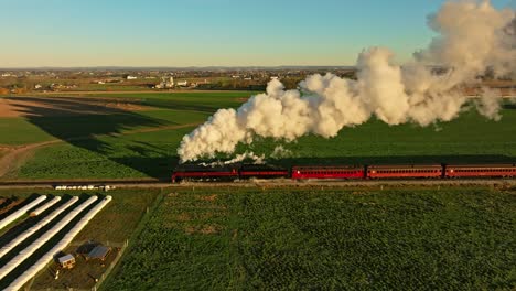 Vista-Paralela-De-Drones-De-Un-Motor-De-Vapor-Que-Sopla-Mucho-Humo-Temprano-En-La-Mañana-Viajando-A-Través-De-Las-Tierras-De-Cultivo