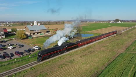 Drone-Ahead-View-of-a-Steam-Passenger-Train-Blowing-Lots-of-Smoke-and-Steam-on-a-Sunny-Fall-Day