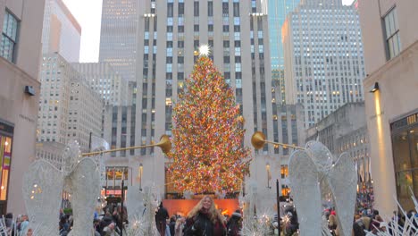Mujer-Alegre-Bailando-En-El-Centro-Rockefeller-Con-Un-Enorme-árbol-De-Navidad-En-El-Centro-De-Manhattan,-Ciudad-De-Nueva-York