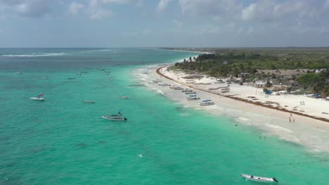 Aerial-flyover-beautiful-beach-and-coastline-of-Tulum-with-parking-boats-on-shore-during-sunny-day,Mexico