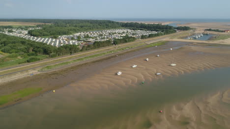 Establishing-Drone-Shot-of-Tidal-Creek-at-Low-Tide-with-Beach-and-Static-Caravan-Homes-in-Wells-Next-The-Year-North-Norfolk-UK-East-Coast