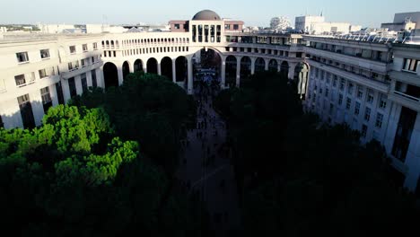 Tilting-drone-shot-of-green-lush-area-in-the-city-of-Montpellier-in-France-with-people-walking-in-a-square-and-birds-flying-by