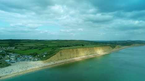 Bridport-West-bay-aerial-rising-view-of-cliffs-above-British-seaside-turquoise-ocean-coastline,-Dorset