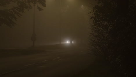 bright-headlights-of-a-single-car-shining-trough-treeline-on-a-misty-night