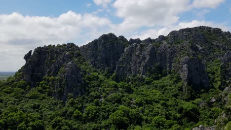 Descending-aerial-footage-revealing-the-limestone-mountains-and-then-the-this-famous-temple,-Wat-Khao-Daeng,-Khao-Sam-Roi-Yot-National-Park,-Phrachuap-Khiri-Khan,-Thailand