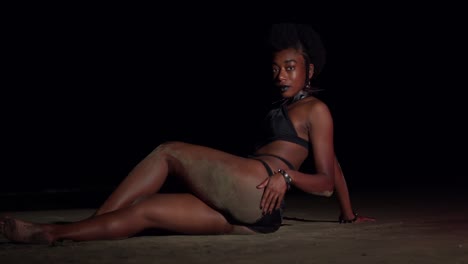 Young-amazing-black-woman-in-a-sexy-bikini-enjoys-laying-in-the-sand-at-night-with-ocean-waves-in-the-background