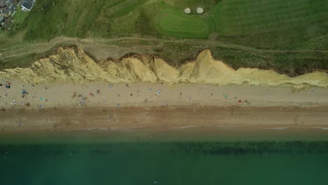 Bridport-West-bay-cliffs-above-British-seaside-turquoise-ocean-coastline-aerial-Birdseye-dolly-right