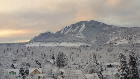 Low-drone-shot-moving-forward-of-Boulder-Colorado-and-rocky-Flatiron-mountains-after-large-winter-snow-storm-covers-trees,-homes,-streets,-and-neighborhood-in-fresh-white-snow