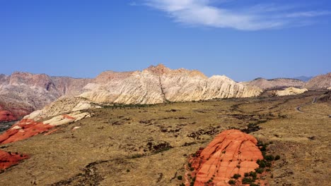 Schöne-Luftdrohnenlandschaft-Natur-Dolly-In-Aufnahme-Von-Großen-Atemberaubenden-Roten-Und-Weißen-Felsformationen-Umgeben-Von-Einem-Tal-Der-Vegetation-Im-Snow-Canyon-State-Park-In-Utah-An-Einem-Warmen-Sommertag
